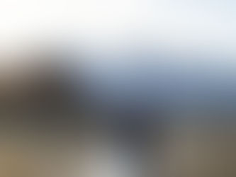 Cowboy and bride kiss in front of rustic barn, with snowy mountains in the background. Golden grass, clear sky, romantic mood.