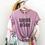 Thumbnail: Purple shirt with black bold text "speak with grace" hanging on a rack with other clothes.