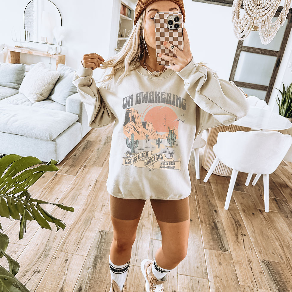 Thumbnail: Woman wearing Cream colored crewneck with muted toned scenery with desert moutains, cacti, and orange sun with "on awakening let us think about the 24 hours ahead" taking a selfie in mirror, with biker shorts, high socks, and tennis shoes, in a living and dining room.