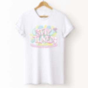 White tshirt with colorful text 'stay tuned' with neon yellow, pink, and green. on a wood hanger.