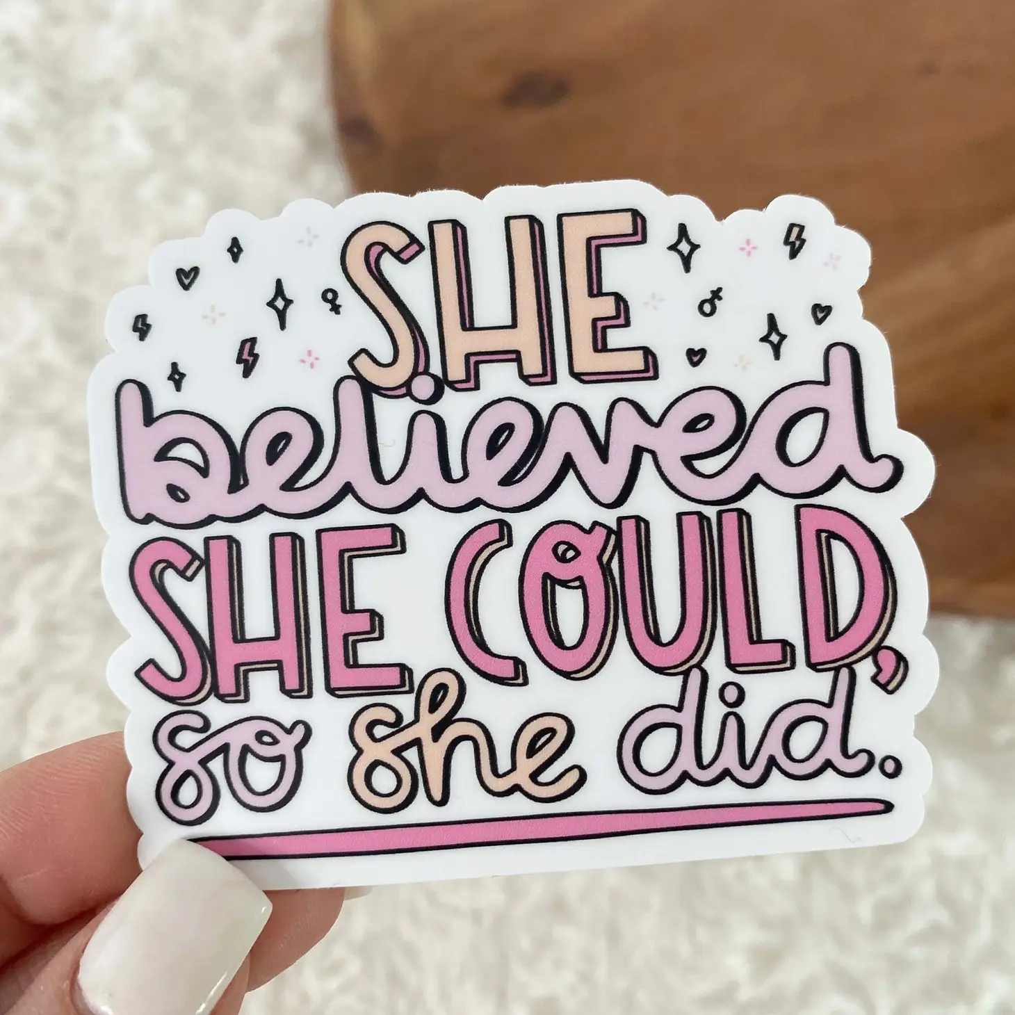 Sticker with pink bubble letters/cursive writing, saying "She believed she could, so she did." with stars and sparkles behind the words.