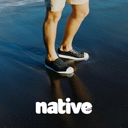 Person wearing black Native slip-on shoes on reflective surface.