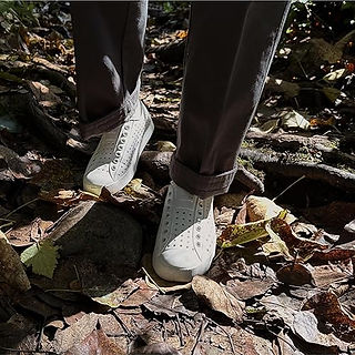 Person wearing white Native shoes walking on a rocky forest floor with fallen leaves.