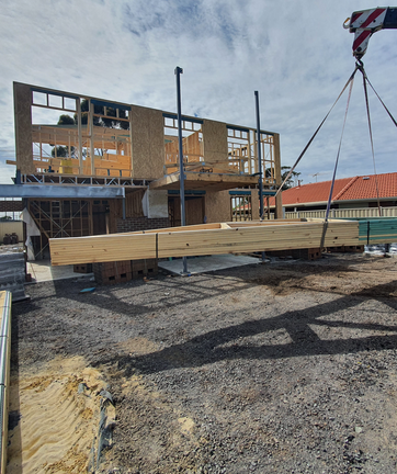 Crane lifting timber beams at house renovation site