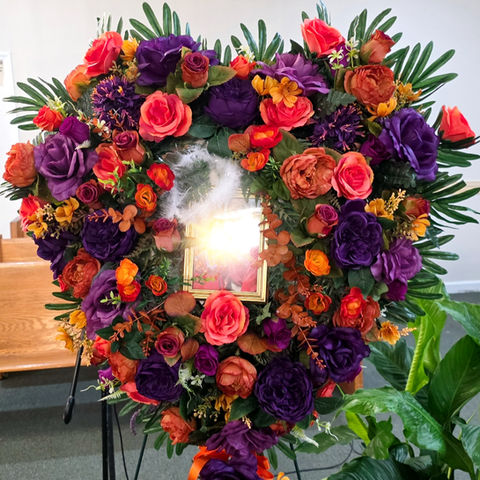 Custom flowers for a funeral with orange, purple, and gold roses shaped into a heart.