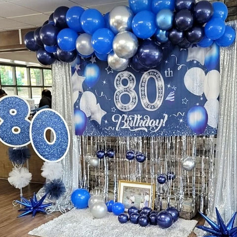 80th birthday event decor with blue and silver balloons and sparkly backdrop.
