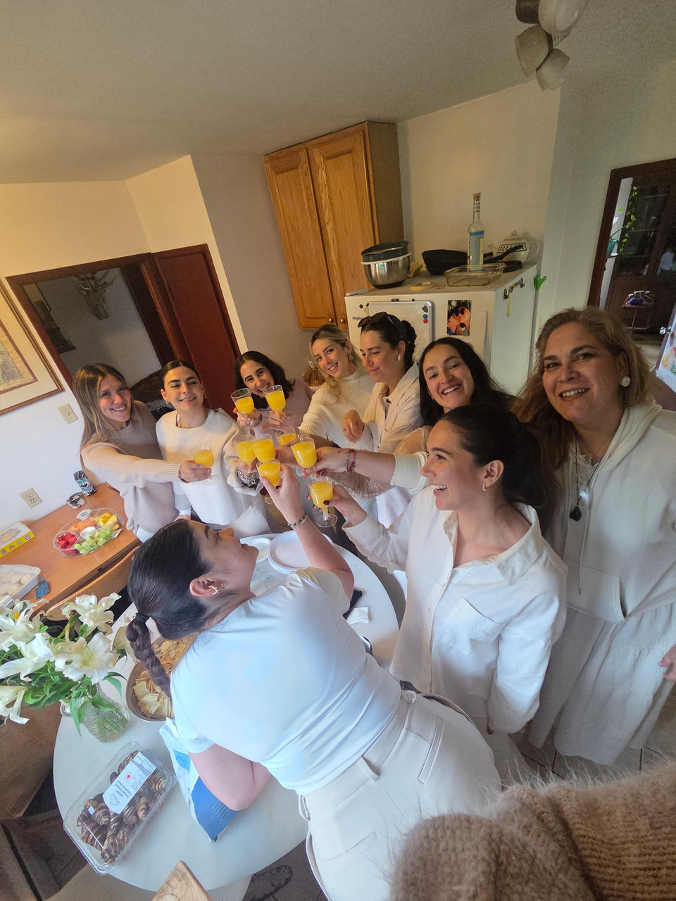 Group of women celebrating cheers with drinks in white outfits