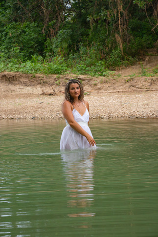 Woman in white dress standing waist deep in river.