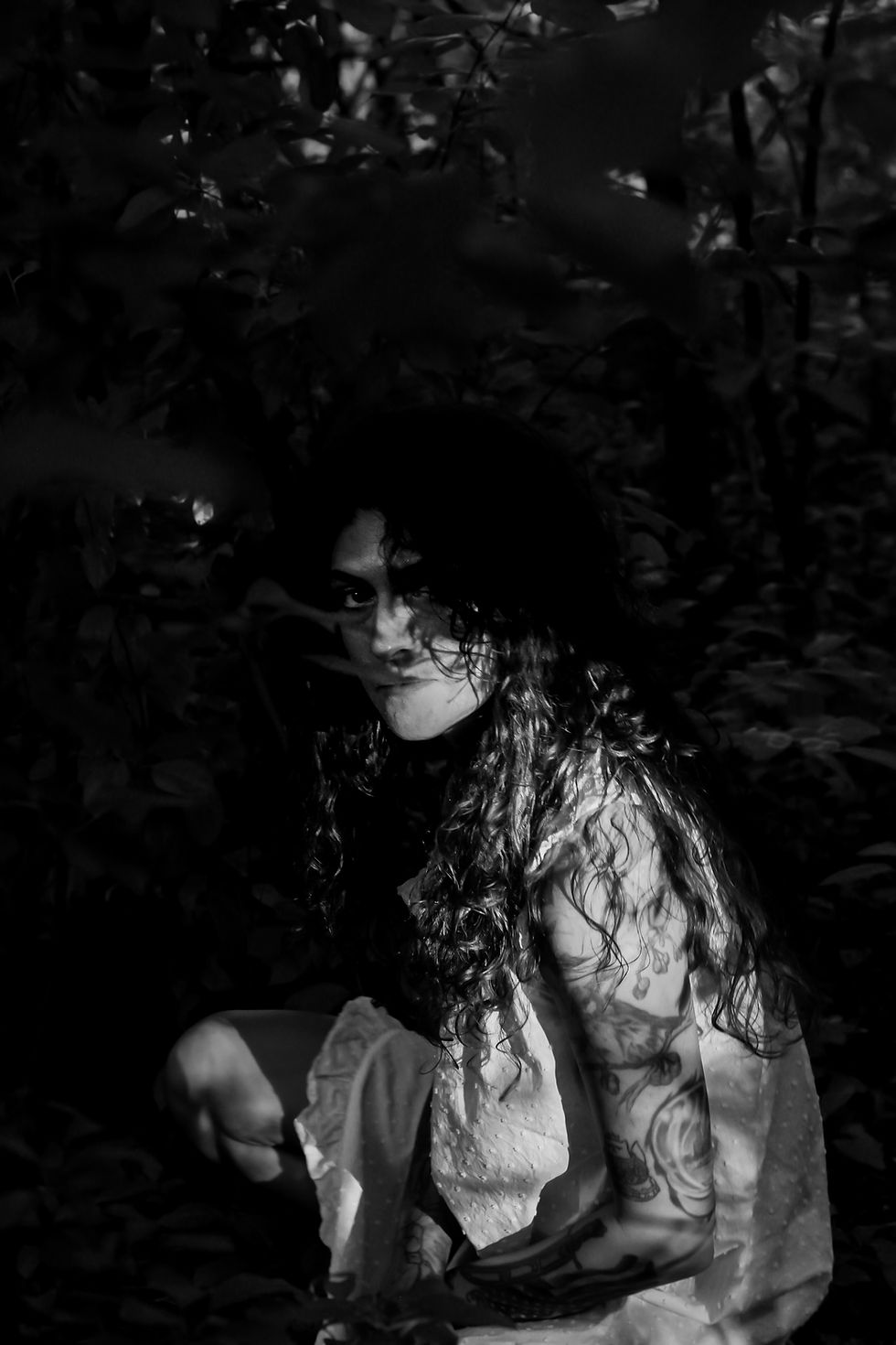 A woman is shrouded in darkness in a grove of trees looking forlorn