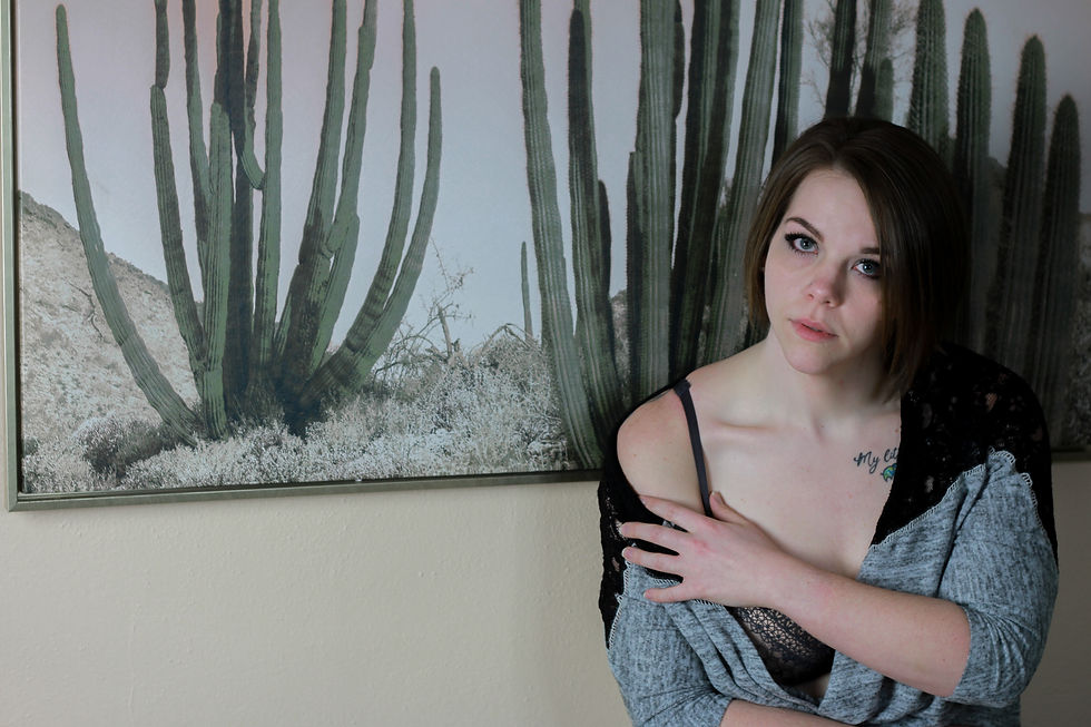 a woman sits in front of a photo of a large cactus with a sweater hanging off her shoulder, looking pensive