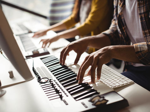 two people playing two keyboards on a desk