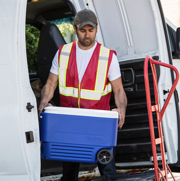 Image of a volunteer carrying an ice chest while wearing the MAX432 volunteer vest in red.