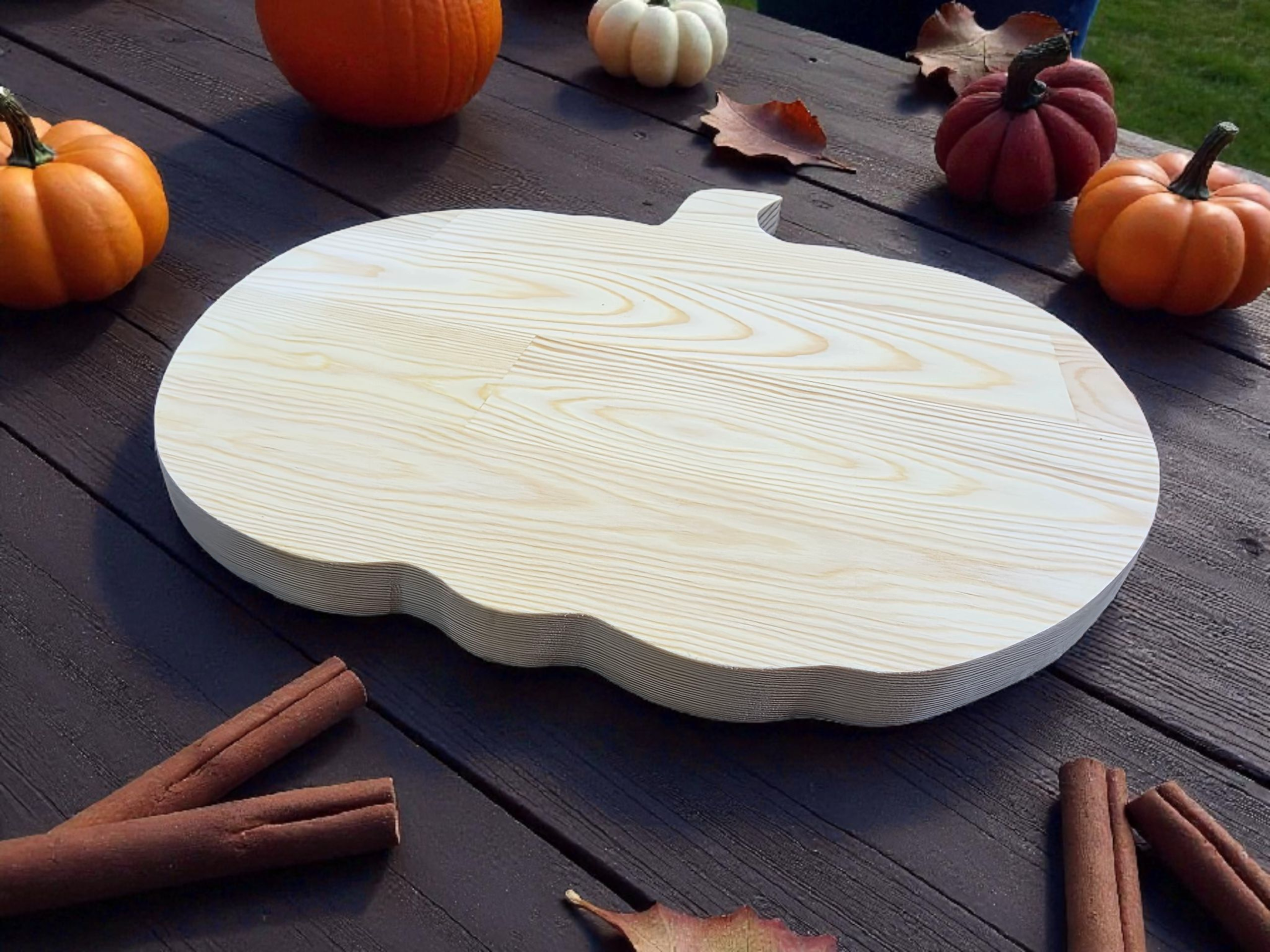 Handmade Wooden Pumpkin Serving Board surrounded by pumpkins and cinnamon sticks on a table.