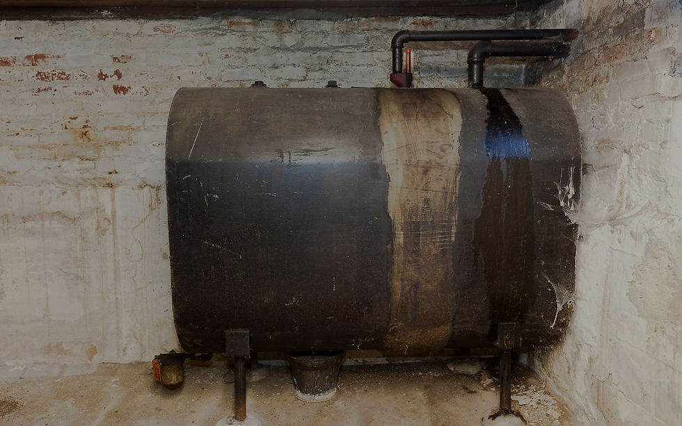 A large black metal oil tank in a basement with exposed piping.