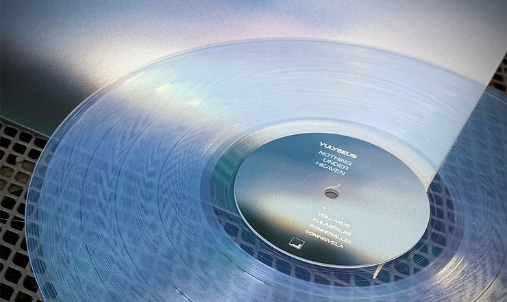 Translucent blue vinyl record titled "Nothing Under Heaven" by Yulyseus, on a turntable. Background has a metallic sheen.