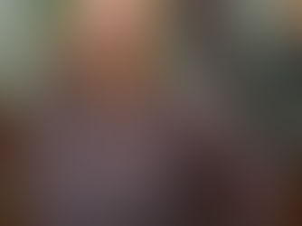 A white woman with a blonde bob and floral blouse smile in front of a multi-colored tile mural.