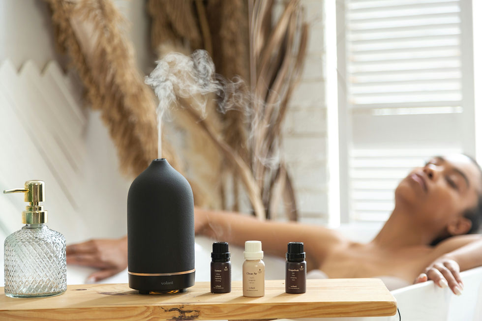 a wooden plank straddling a bath tub with a diffuser dispensing mist and three essential oil bottles. a black woman is soaking in the tub