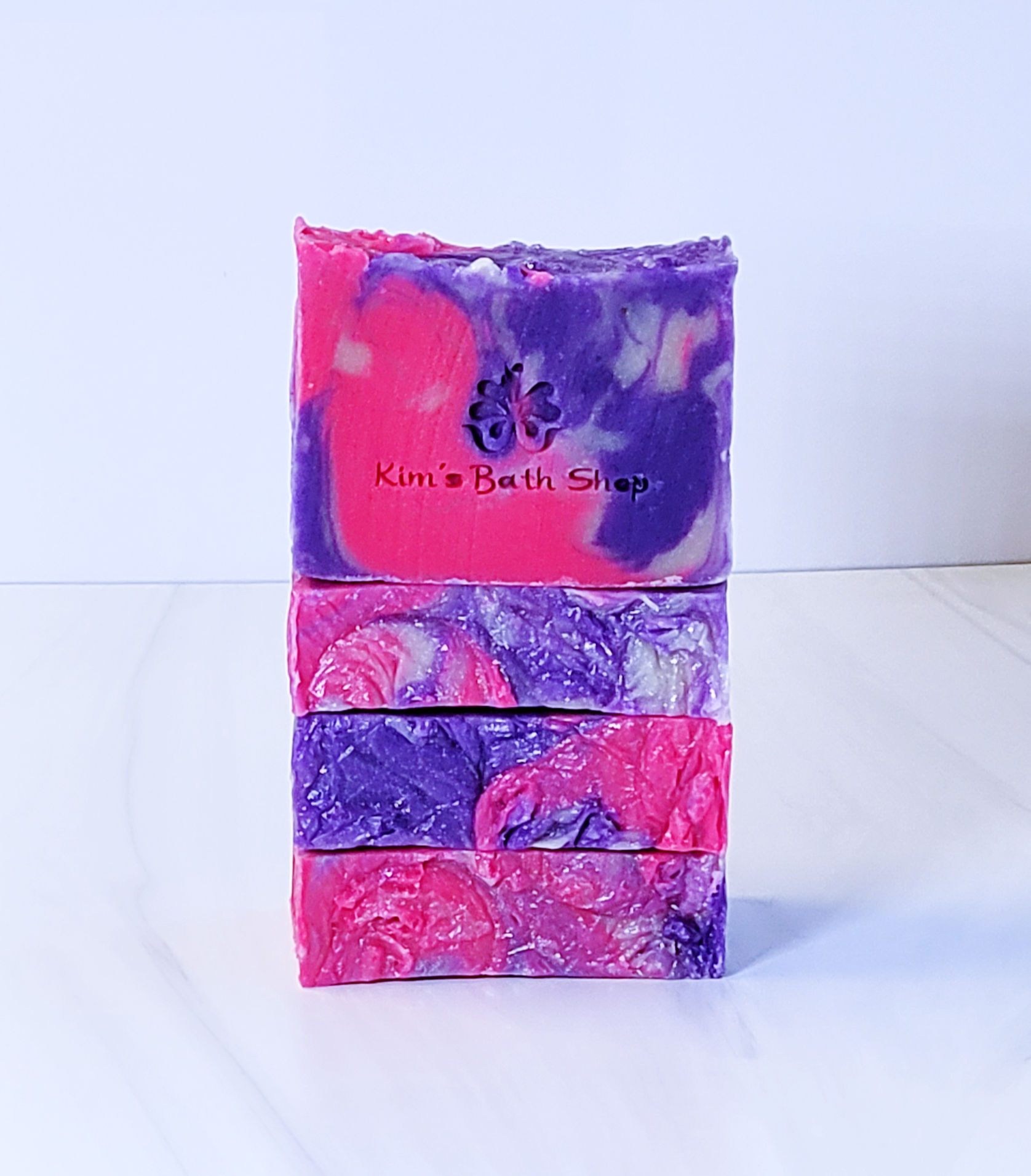 Stack of handmade, swirled pink and purple soap bars with a butterfly logo, labeled "Kim's Bath Shop"