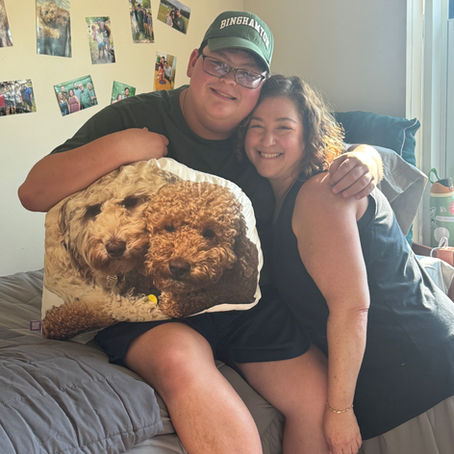 Rafi and his mom hug on his new college bed, Rafi holds a pillow containing the faces of his two dogs.