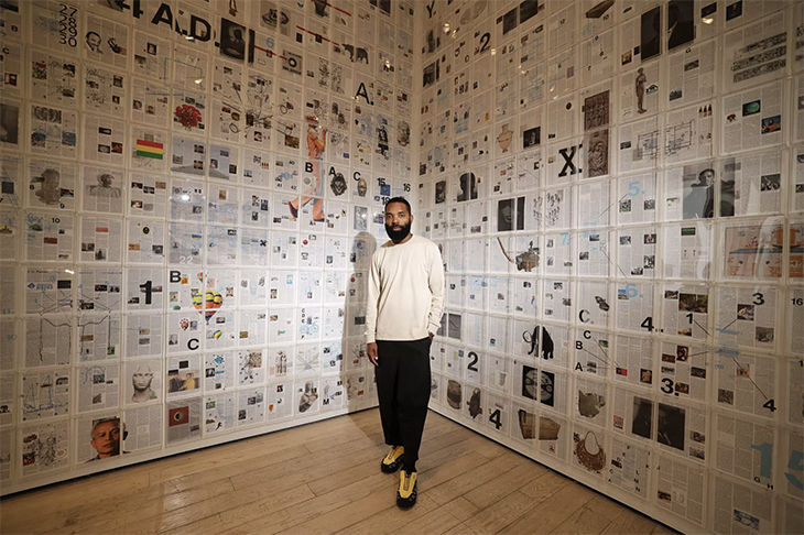 Tavares Strachan poses with his installation “Six Thousand Years,” which is made up of 2,000 panels from his “Encyclopedia of Invisibility.” The leather-bound tome contains 17,000 entries that the artist wrote to bring attention to little-known facts and Black trailblazers. Courtesy of Allen J. Schaben / Los Angeles Times.