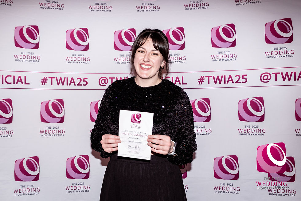 A woman stands in front of a printed background that says The Wedding Industry Awards. She smiles and holds up a certificate in front of her.