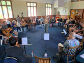 Large group of musicians playing in a circle with Claudia Bulaievsky standing in the middle of the circle