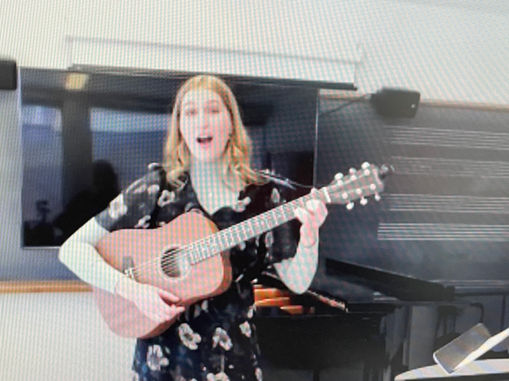 A screenshot of Emma singing and playing guitar in her lecture recital that someone was watching via Zoom.