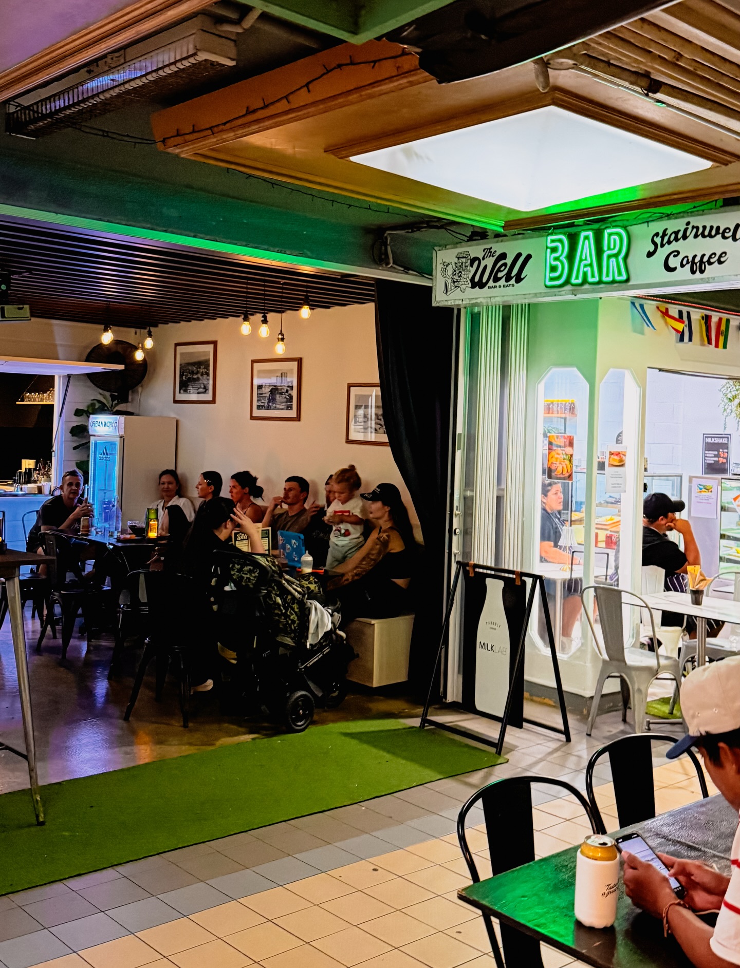 The Well’s green neon BAR sign, tables and arcade seating