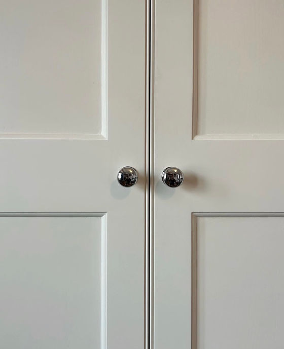 Close-up of painted wardrobe doors with chrome knobs and traditional panel moulding.