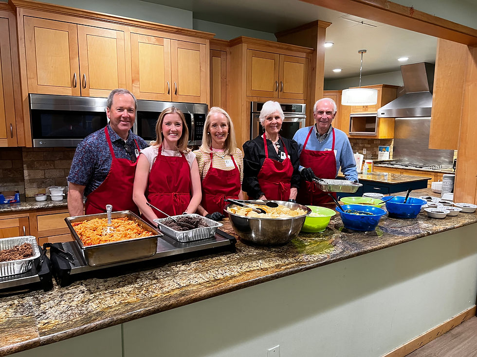 Five people in red aprons serving food in a kitchen