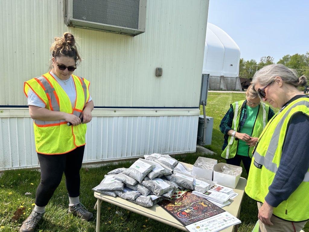 Maria stands in front of a table with posters and small bags of compost for residents to take home.