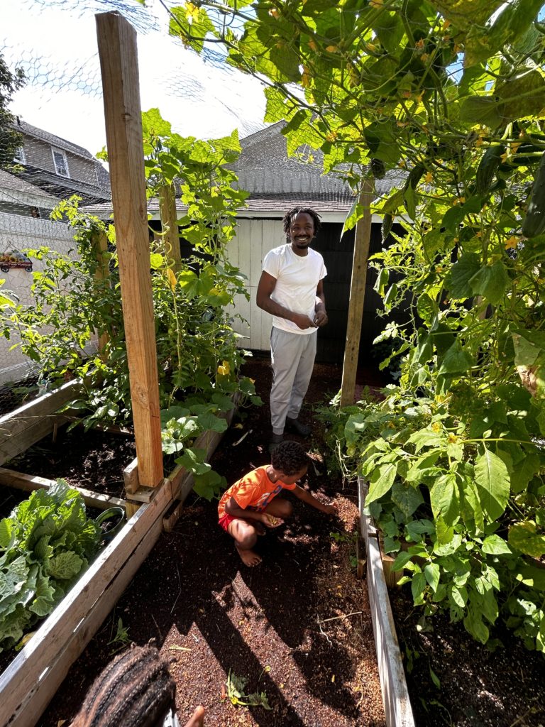 Lamont stands under his hanging garden of cucumbers while Tre picks up fallen cucumber blossoms.