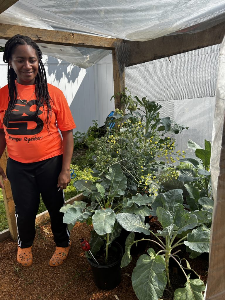 Bria poses with her cole crops, growing in the shade for fall planting.
