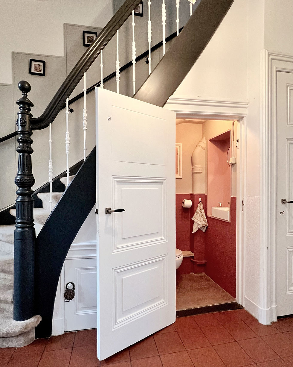 Trap met zwart-witte balustrade naast open witgeschilderde deur die naar een kleine roze toiletruimte leidt. Gemoedelijke sfeer.