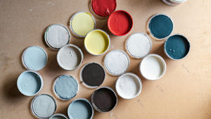 Open paint cans on a wooden surface, displaying a variety of colors: red, yellow, blue, and white. Numbers are written near each.