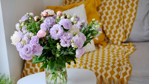 A vase of pink and purple flowers on a white table, set against a cozy sofa with a yellow zigzag blanket. Bright, cheerful atmosphere.
