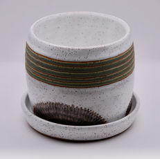 Cylindrical planter made with speckled clay glazed in white with green and copper decor.  Green overlaps horizontal strips near the top rim.  Copper overlaps a carved semi-circle near the pot bottom.  Includes a matching base.  