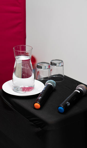 Two wireless microphones with colored markers placed on a black table beside a glass jug of water and two empty glasses.