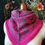 Thumbnail: A knitted colourwork cowl displayed on a mannequin. It is bright pink and dark grey with spider and cobweb motifs