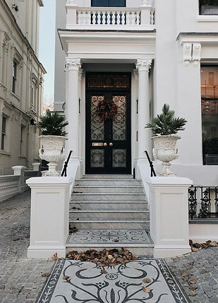 White entrance with stairs and plants leading to a black door Hostroo.