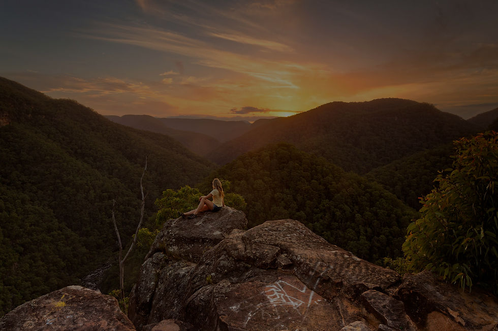 A woman sits on a rock while the sun sets, she's confident and at peace.