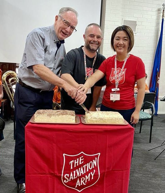 Colonel Kelvin Merrett (left) cuts the celebration cake with Richmond Corps Officers Major Craig Farrell and Captain Ellen Farrell.