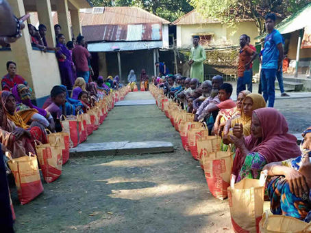 Community members seated in orderly rows during what appears to be a food or aid distribution event in an outdoor courtyard setting.