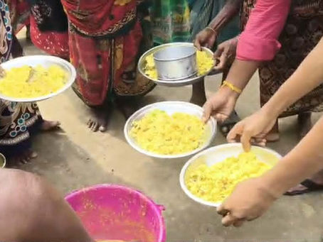 "Volunteers serving dal into metal plates and bowls for a group of women in colorful saris during a community food distribution."