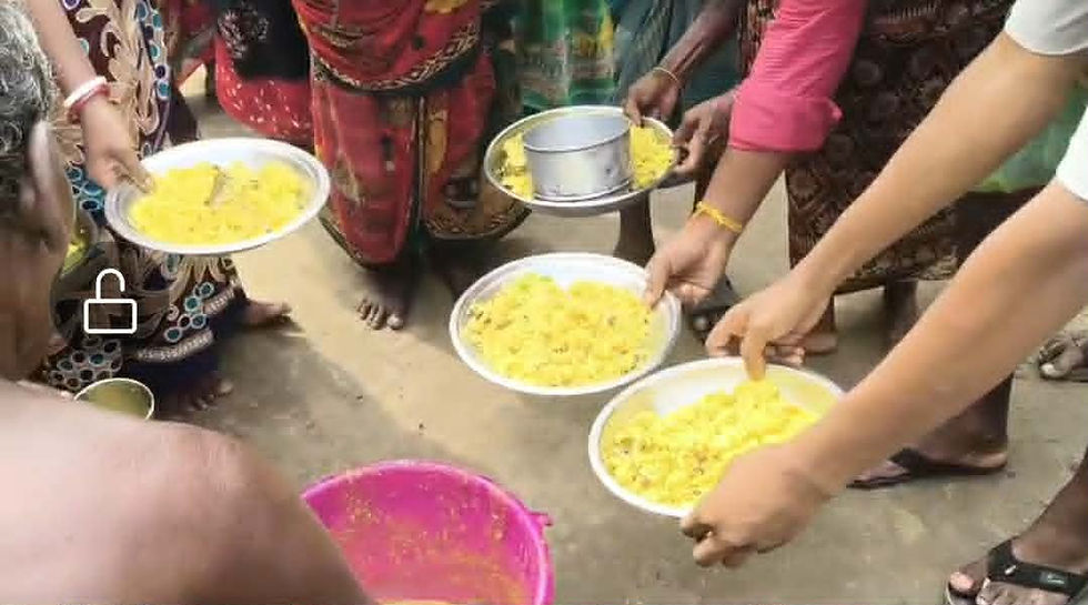 "Volunteers serving dal into metal plates and bowls for a group of women in colorful saris during a community food distribution."