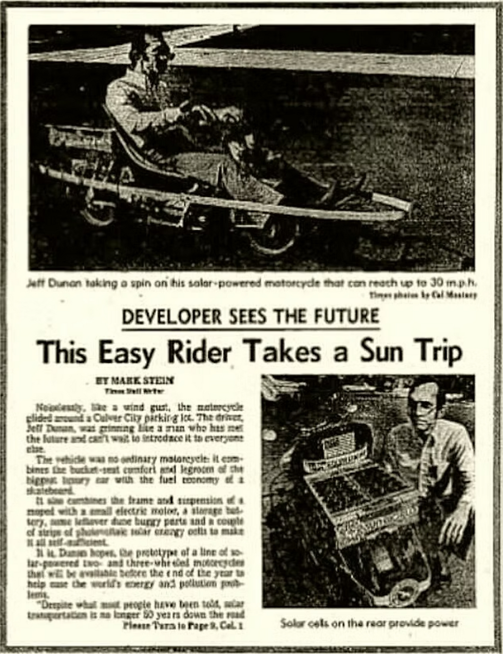 A newspaper article clipping titled "DEVELOPER SEES THE FUTURE: This Easy Rider Takes a Sun Trip" featuring two black-and-white photos: one showing Jeff Dunan driving a low-profile solar-powered motorcycle, and another showing him kneeling beside the vehicle's rear solar cells.