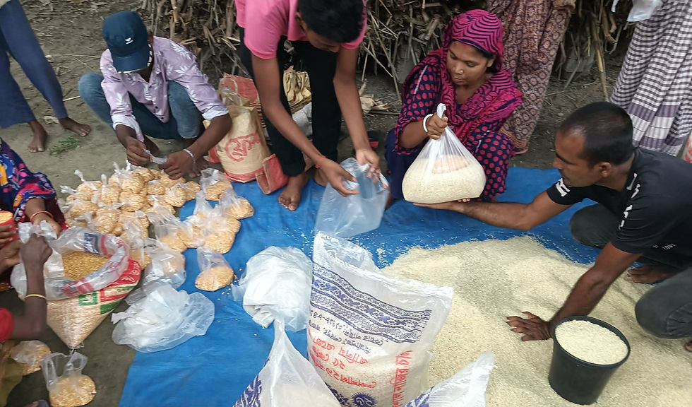 "Volunteers sit around a blue tarp outdoors, scooping white rice from a large pile into plastic bags using a measuring bucket, with dozens of pre-packaged lentil portions and bulk rice sacks arranged nearby during food relief preparation in Bangladesh."