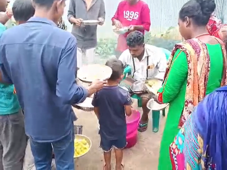 A group of adults and a young child gather outdoors to receive hot meals served onto metal plates during a community food distribution event supported by Lotus Ministry.