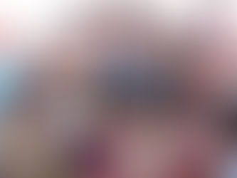 A large group of smiling children crowded together looking at the camera. Many are holding and eating what appears to be bread or flatbread. The children are wearing colorful clothing in various patterns including stripes, florals, and solid colors. They appear to be outdoors in bright daylight, and their expressions show joy and excitement as they gather closely together for the photo.