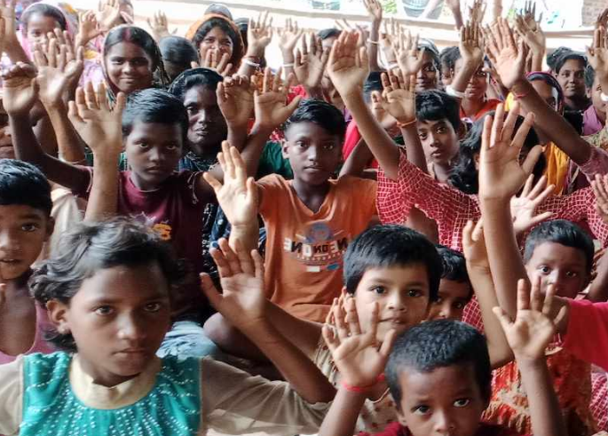 A large group of children and young people enthusiastically raising their hands in the air, appearing to be participating in an interactive activity or responding to a question. The children are wearing colorful clothing including orange, red, green, and other bright colors. They appear to be seated or gathered closely together, with expressions of engagement and excitement on their faces. The setting appears to be indoors, possibly in a classroom, community center, or educational program. The scene captures a moment of active participation and enthusiasm among the young participants.RetryClaude can make mistakes. Please double-check responses.
